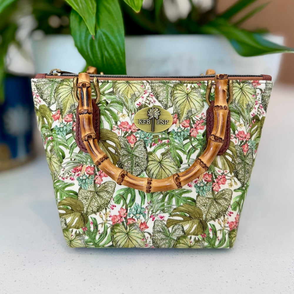 Tropical patterned handbag with bamboo handle on a white surface