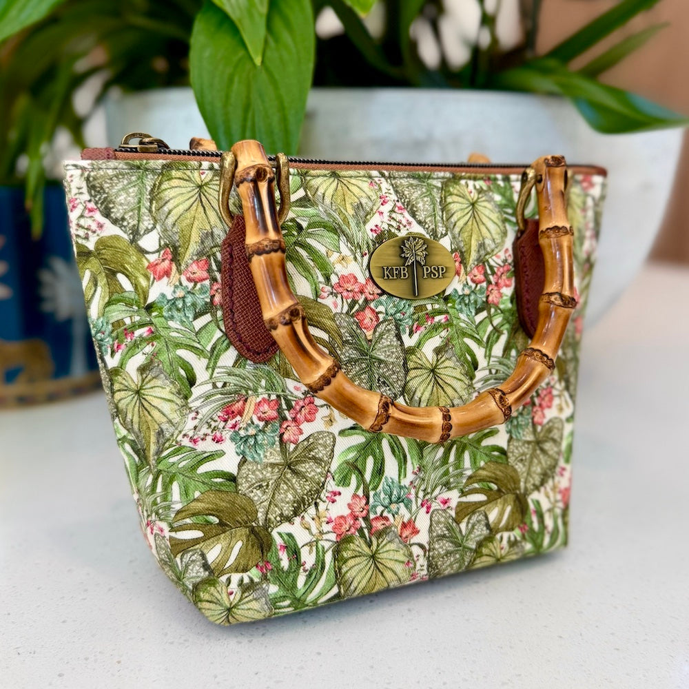 Floral patterned handbag with bamboo handles on a white surface